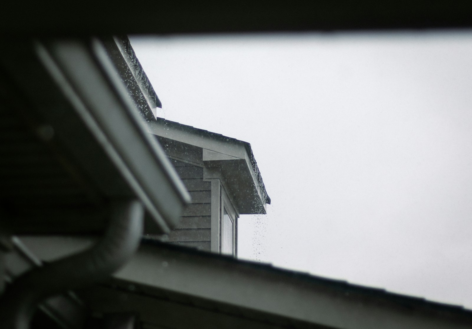 Rain pouring past an overflowing gutter on the roofline of a vinyl-sided home during a storm